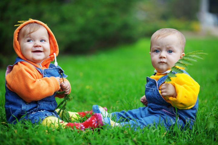 To små børn i klapbukser sidder på en græsplæne.