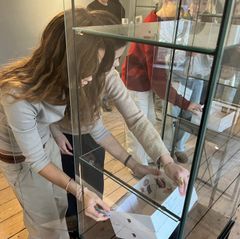 To piger placerer en model i en glasmontre.