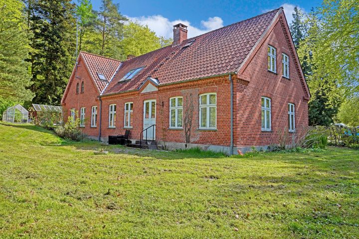 Rødt murstenshus med stor have og skov i baggrunden.