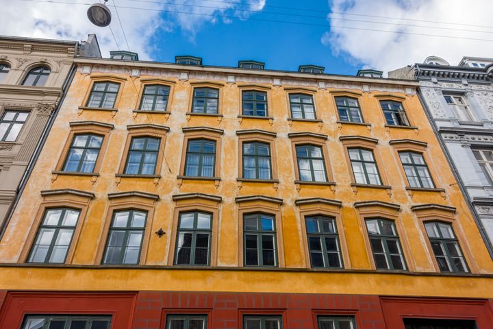 En lys, gammel bygning med mange vinduer under en blå himmel.