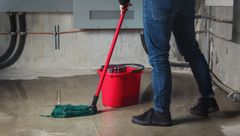 Person mopper et vådt gulv i en kælder med en rød spand.