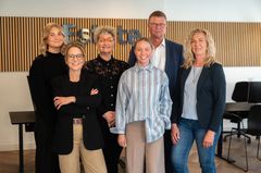 Alt tekst: Gruppefoto af et team fra Estate Glamsbjerg. Seks personer står smilende foran en væg med et skilt. En person omtales, men er ikke til stede på billedet.