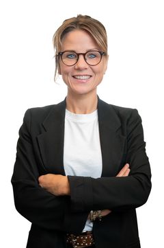 Line Møller, Estate-ejendomsmægler i hvid t-shirt iført en sort blazer, står med armene over kors og smiler.