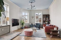 Stue med moderne indretning, herunder en rød sofa, blå lænestol, lys tæppe og et fladskærms-tv på væggen.