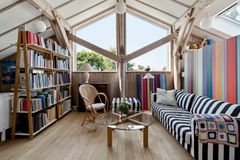 Lyst rum med skrå loft, stribede møbler, bogreol og glasbord.