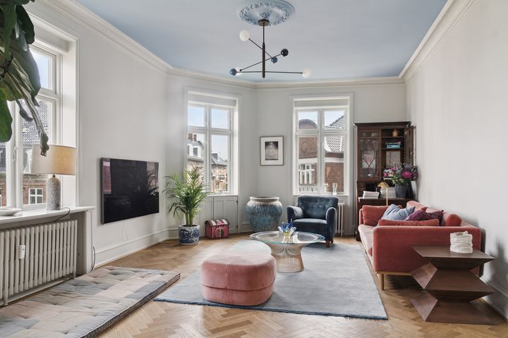 Stue med moderne indretning: blåt loft, rød sofa, blå lænestol og store planter.