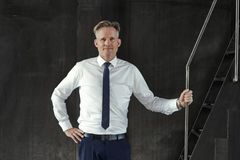 Mand i skjorte og slips står ved en trappe med en hånd på gelænderet.