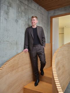Mark Andersen, Indehaver af &LIVING i Aalborg iført mørkt jakkesæt går ned ad en trætrappe med buet gelænder i en moderne bygning.