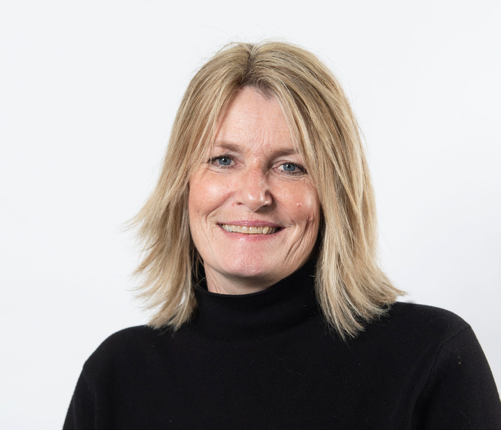 Birgit S. Hansen, KL, iført en sort trøje, der smiler mod kameraet med en hvid baggrund.