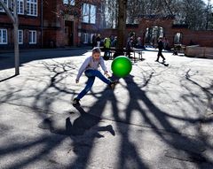 Børn i leg i en skolegård. En dreng midt i billedet sparker en fodbold i retning af fotografen.