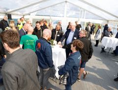 Omkring 90 gæster deltog i fejringen og indvielsen af Bjørnstrup Vindmøllepark, som leverer strøm svarende til 20.000 husstandes forbrug. Gæster står i et telt ved højborde og snakker og spiser mad.
