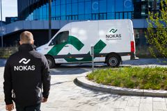 Person i NOKAS-uniform går mod en hvid NOKAS-pengetransportvogn parkeret foran en moderne bygning.