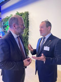 Manfred Weber og Jeppe Hedaa i jakkesæt i samtale foran en grøn væg i et kontor.