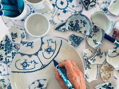 Skår af blåmalet porcelæn og hånd der maler på tallerken