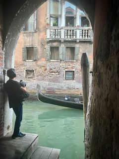 Lydkunstneren står med optageudstyr under en muret bue ved en kanal med grønligt vand i Venedig