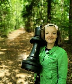 Katrine Møller Mathiesen står på en skovsti og smiler, mens hun holder et stort skakbrik.