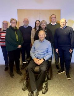 Gruppefoto af rådet, som står foran en væg. Forrest ses Jess Eiberg Hansen, formand, som sidder i kørestol.