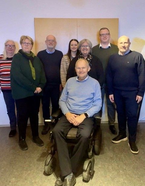 Gruppefoto af rådet, som står foran en væg. Forrest ses Jess Eiberg Hansen, formand, som sidder i kørestol.