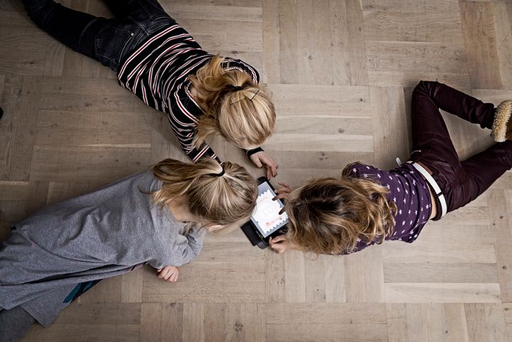 Tre børn ligger på gulvet og ser på en tablet sammen.