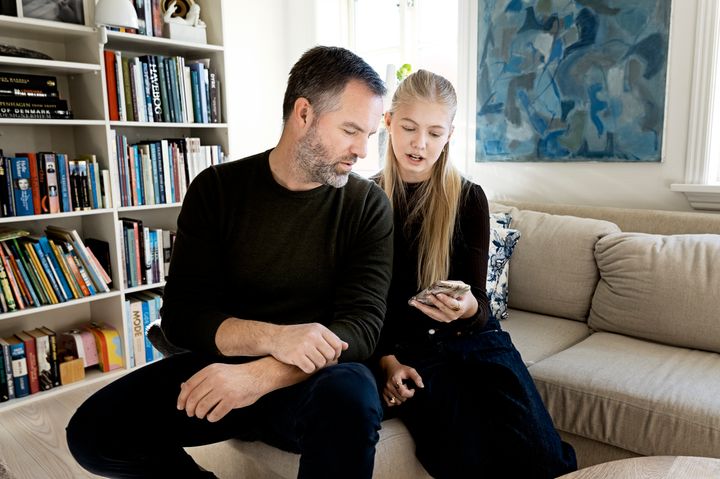 En mand og en pige sidder i en stue, mens de kigger på en mobiltelefon.