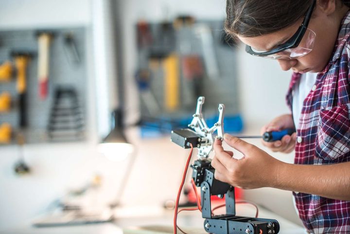En person arbejder på en robotarm med værktøj i et værksted.