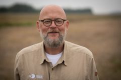 Billedet viser en mand med skæg, briller og en skjorte med logoet "Hempel Fonden", stående i et udendørs, naturagtigt miljø.