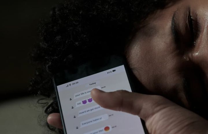 Ung kvinde ligger ned og græder med sin telefon i hånden, der viser ubehagelige beskeder