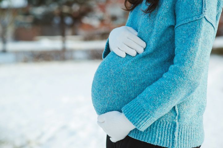 Gravid kvinde iført blå sweater holder på sin mave