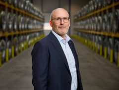 Jacob Vesterlund Otto står i jakkesæt står i en lagerbygning med rækker af hylder i baggrunden.