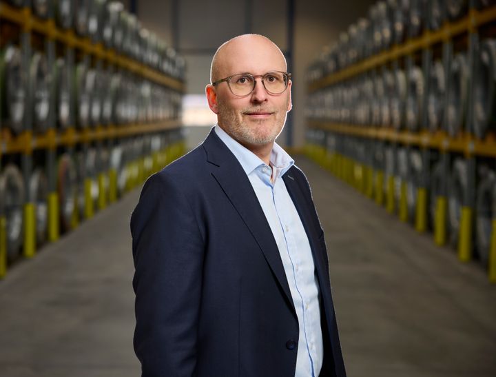 Jacob Vesterlund Otto står i jakkesæt står i en lagerbygning med rækker af hylder i baggrunden.