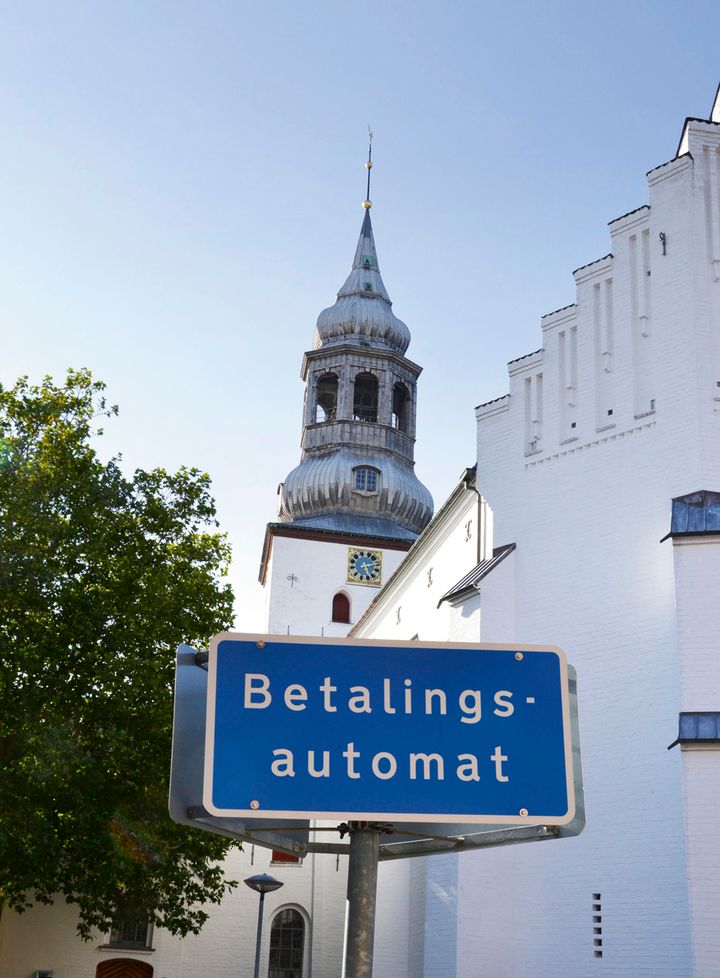 Blåt skilt med betalingsparkering og kirketårn i baggrunden