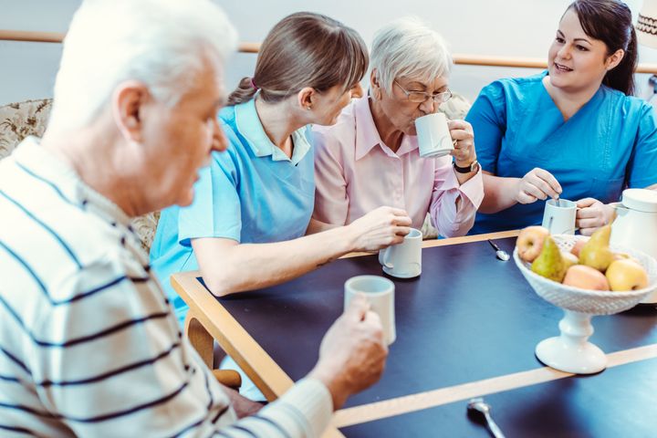 To ældre sidder ved et bord sammen med to hjælpere på et plejehjem.