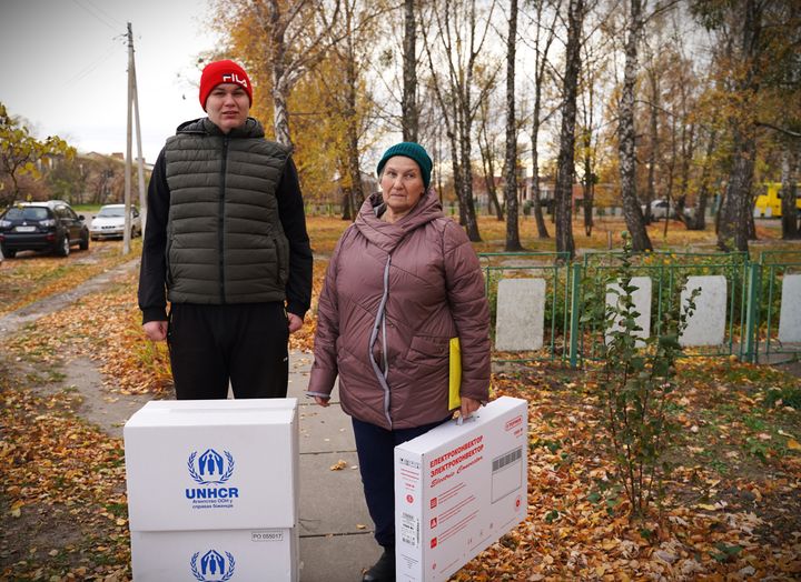 To personer står udenfor og holder kasser med UNHCR-udstyr til vinterisolering.