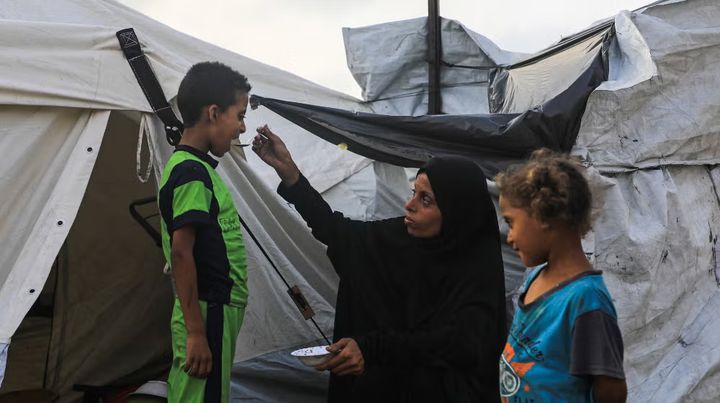 En kvinde giver sine børn mad foran deres telt i en flygtningelejr i det vestlige Gaza City.