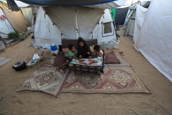 A woman sits with her three children beside their family tent in a displacement camp in western Gaza city; her baby is just two months old.