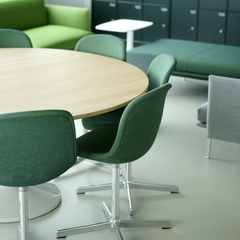 En lys og moderne lounge med grønne stole omkring et rundt træbord.