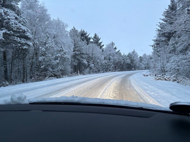 Bil kører på sneklædt vej omgivet af træer dækket med sne.