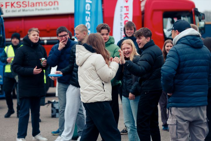 Unge mennesker står sammen og smiler foran store lastbiler ved Logistikkens Dag.