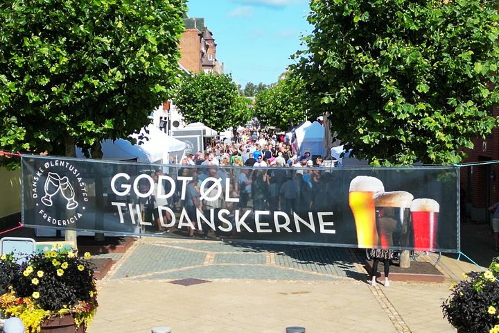 Et banner med teksten "Godt øl til danskerne" hænger over en gade fyldt med mennesker og boder.