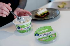 Billedet viser en ung kvionde, som med en ske er ved at øse hytteost op fra et bæger til en tallerken med en rugbrød og avokado.
