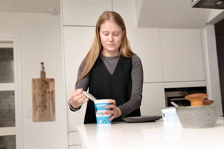 Billedet viser en ung kvinde, der åbner et bøger med hytteost.