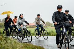 En gruppe mennesker cykler i regnvejr. Nogle bærer regnjakker, andre regnslag og en person cykler med en udslået gul paraply