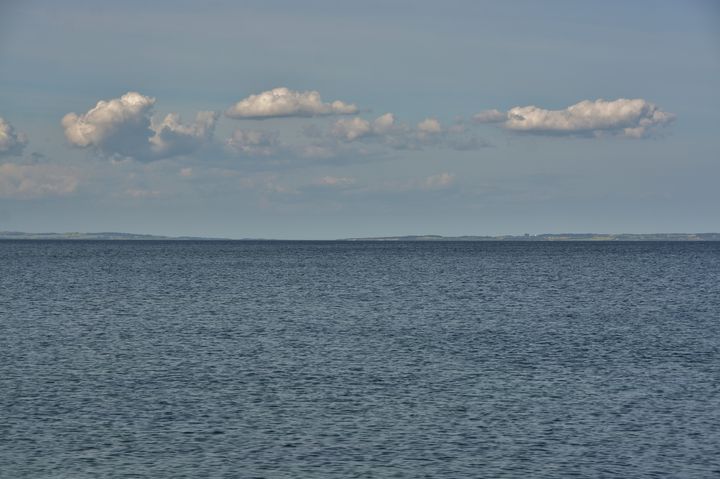 Roligt hav med blå himmel og spredte skyer.