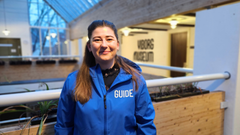 En kvinde iført en blå jakke med teksten "Guide" står indendørs på Viborg Museum.