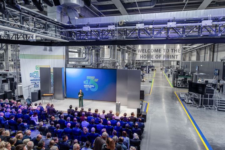 A speaker addresses an audience at the opening of Heidelberg's customer demonstration center with banners celebrating their 175th anniversary.