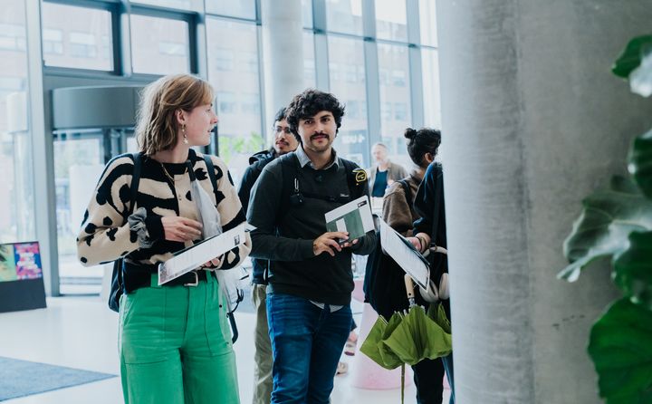 To studerende, en kvinde og en mand, står og taler sammen i en aula