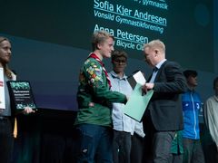 En person i en spejderuniform modtager håndtryk og diplom.
