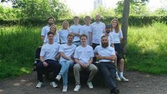 En gruppe mennesker iført hvide "Leaf" t-shirts sidder og står udendørs i et grønt område.