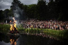 Folk samlet omkring et Skt. Hans bål ved en sø.