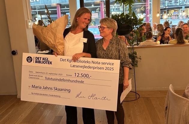 To kvinder står sammen, hvor den ene holder en stor check og blomster.